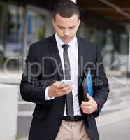 A handsome young mixed race business man using his cellphone while walking through the city on his way to work. Young and confident corporate professional checking messages during his morning commute
