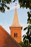 Low angle of a church bell tower against a blue sky. Exterior view of a traditional old religious red brick building on a sunny day. Wall and roof of an historic house or home architecture design