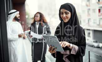 One touch is all it takes. an attractive young businesswoman dressed in Islamic traditional clothing using a tablet on her office balcony.