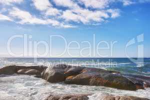 Landscape of large rocks in the ocean with a cloudy blue sky and copy space. Sea waves splashing against boulders on popular Camps Bay beach in Cape Town, South Africa. A beautiful summer destination