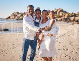 Portrait of a happy african american family with two children standing together on the beach. Loving mother and father carrying their daughter and son while spending time together on vacation