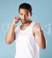 Handsome young hispanic man in a boxer pose standing in studio isolated against a blue background. Mixed race male athlete wearing a vest, ready for a fist fight or boxing match. A confident sportsman