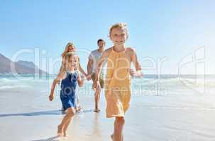 Joyful young family with two children running on the beach and enjoying a fun summer vacation. Two energetic little girls having a race while their mother and father follow in the background