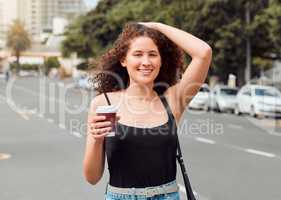 Portrait of a happy beautiful young mixed race woman exploring the city while holding a takeaway coffee and touching her curly brunette hair. Hispanic tourist enjoying the view downtown on the weekend