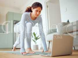 Beautiful young mixed race woman using a laptop to follow an online class while practicing yoga at home. Hispanic female exercising her body and mind, finding inner peace, balance and clarity