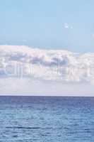 A cloudy blue sky and peaceful, calm ocean separated by a beautiful horizon with copy space. Deep blue water underneath a cloudscape skyline. The many tides, currents and waves in the wide open sea
