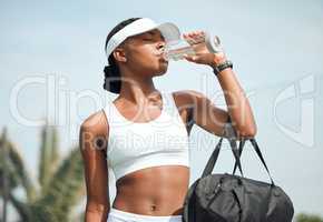 Got to stay hydrated to perform well. a sporty young woman drinking water while playing tennis outdoors.