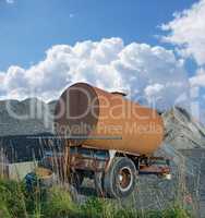 Old water tanker decaying at construction site. Rusted water container near a heap of concrete and cement. Abandoned old rusty water trailer tank near a pile of sand and gravel in building industry