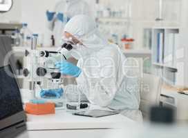 Its clear to see now. a scientist wearing a radiation suit while using a microscope in a lab.