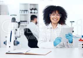 Portrait of young happy african american medical scientist with an afro using a digital tablet to record test results from a microscope. Mixed race chemist discovering a vaccine cure in a laboratory