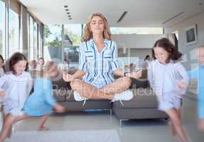 Young mother meditating for stress relief while her energetic kids run around her. Calm mom with naughty mischievous children running around her in the living room at home