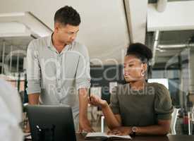 Two multiethnic businesspeople talking at a desk discussing online project on laptop. Mentor and colleague explaining and brainstorming ideas with colleague in modern office