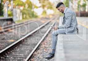 Making moves for his next ticket to success. a young businessman using a cellphone while sitting alongside a railway track during his commute.