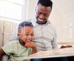 African american father bonding with his at home. Black male helping his son read a book and practice learning while sitting on a sofa at home. cute little black boy reading to his dad in the lounge. father and son smiling while learning some educational 