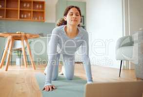 Beautiful young mixed race woman using a laptop to follow an online class while practicing yoga at home. Hispanic female exercising her body and mind, finding inner peace, balance and clarity