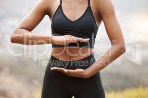 One african american female framing her stomach with her hands while standing outside in nature. Dedicated black woman training and exercising outside to increase her health and fitness levels