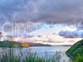 Scenic view of a lake, ocean or sea with cloudy sky at sunset and copy space.Uncultivated trees, bushes, shrubs around a bay of water in Norway. Landscape of calm, serene, peaceful, quiet nature pond