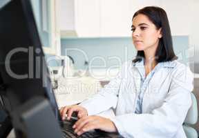 One confident and focused young caucasian doctor using a computer to browse the internet in a clinic. A medical professional wearing a labcoat and updating patient reports on a desktop in her hospital