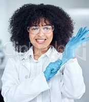 Portrait of young african american female scientist with afro hair wearing a labcoat and goggles while putting on gloves in the laboratory. A mixed race female scientist getting ready to conduct an experiment
