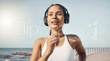 Happy young fitness woman in sportswear wearing wireless headphones and listening to music while out for a run along the promenade. Exercise is good for you health and wellbeing
