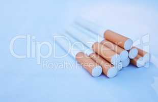 Closeup of a pack of cigarettes isolated on a blue background. Macro view of a group of tobacco cigarettes stacked together and lying down. Smoking addiction is unhealthy and harmful to wellbeing