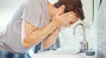 One handsome man washing his face in a bathroom at home. Caucasian male using a face wash to prevent breakout, acne and blemishes in his apartment