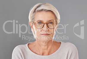 One mature caucasian woman wearing trendy brown prescription spectacles against a grey copyspace studio background. Senior female looking serious wearing reading glasses for better eyesight