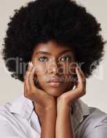 Studio portrait of a young stunning African American woman with a beautiful afro. Confident black female model showing her smooth complexion and natural beauty while posing against a grey background