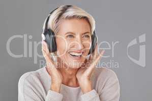 One happy mature woman isolated against a great background in a studio and wearing headphones to listen to music. Smiling caucasian senior with grey hair enjoying the loud music. Youthful and playful