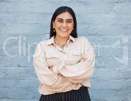 One young business woman of indian ethnicity standing outside against a grey wall with her arms crossed. Happy and confident mixed race executive looking positive and successful. Focus and ambition