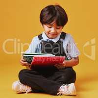 One cute little asian boy sitting on the floor wearing casual clothes while reading against an orange background. Happy and content while focused on education. Child ready for school