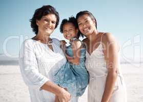 Smiling mixed race family standing together on a beach. Happy hispanic grandmother bonding with granddaughter over a weekend. Adorable little girl enjoying free time with single mother and parent