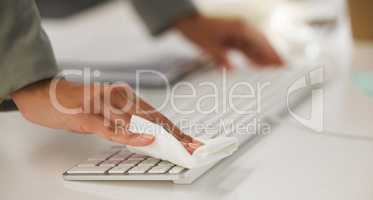 Businessperson holding a tissue and cleaning their computer keyboard while working in an office. Business professional wiping their keyboard to protect from disease