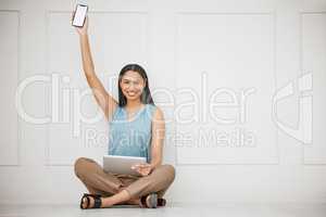 Smiling young businesswoman using a wireless tablet device and holding a smartphone up. Portrait of a business professional working from home sitting on the floor against a white background