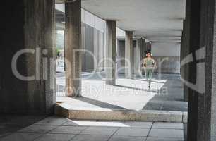 Young hispanic female athlete wearing headphones while running though a building outside. Young sportswoman focused on her speed, body, fitness and cardio health while training