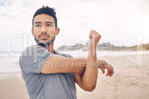 Experiencing an improved mental focus and commitment. Shot of a sporty young man stretching his arms while exercising on the beach.