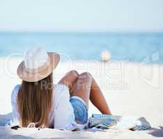 Rearview beautiful young caucasian woman relaxing on the beach. Enjoying a summer vacation or holiday outdoors during summer. Taking time off and getting away from it all. Spending the day alone