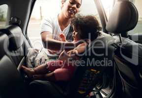 Doing it all by herself. a young woman strapping her baby into her car seat.