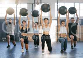 Diverse group of active young people doing overhead medicine ball lunge exercises while training together in a gym. Focused athletes challenging themselves by holding weighted equipment to build muscle and endurance during a workout in a fitness class