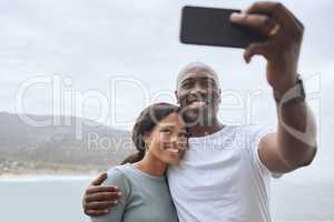Handsome african american man and his beautiful wife taking selfies with a phone against a scenic seascape background. A black woman and her happy husband taking pictures while out hiking in nature