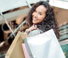 Portrait beautiful mixed race woman standing on an escalator while shopping in a mall. Young hispanic woman carrying bags, spending money, looking for sales and getting in some good retail therapy