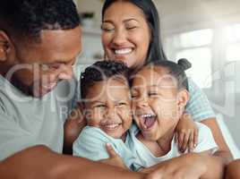 Happy funny mixed race family with two children wearing pyjamas and sitting together embracing each other at home. Cheerful parents sitting with their daughter and son laughing and having fun in the morning