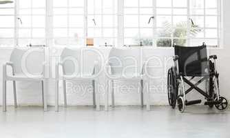 Wheelchair at the end of a row of white chairs in a waiting room. Wheelchair at the end of a row of white chairs in a waiting room.