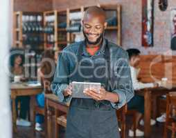 Young african american businessman wearing a apron working in a retail store using a digital tablet device. Portrait of a smiling small business owner, entrepreneur buying stock online using wireless technology in a cafe