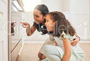 I can feel the excitement increasing. a young mother and daughter checking on their baked goods through the oven door together.