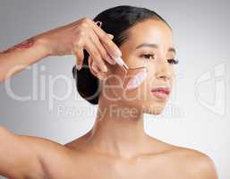 A beautiful mixed race woman using a rose quartz derma roller during a selfcare grooming routine. Young hispanic woman using anti ageing tool against grey copyspace background