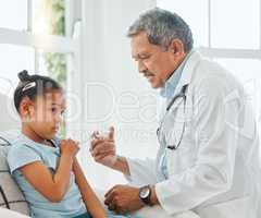 Its better if you look away. Shot of a mature male doctor giving a little girl an injection during a checkup at home.