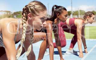 Three female athletes at the starting line in a track race competition at the stadium. Young sporty women in a race waiting and ready to run. Diverse sportswomen at the sprint line or starting blocks