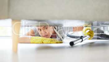 A mixed race domestic worker looking while lying on the floor and cleaning under the sofa. One mixed race female using a vacuum cleaner under a couch to begin spring cleaning