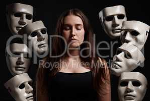 Im in control of my own emotions. Studio shot of a woman standing with her eyes closed while surrounded by masks.